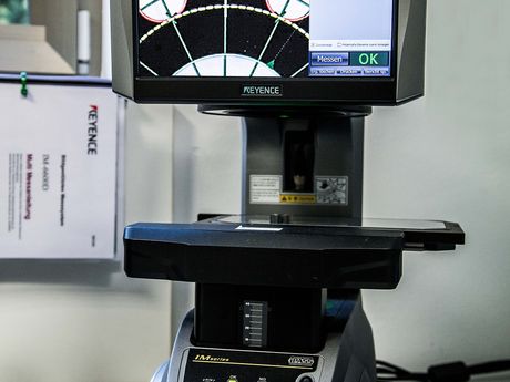 KEYENCE Bildmessgerät mit Monitor, auf dem eine erfasste Bauteilkontur mit Toleranzband erscheint.